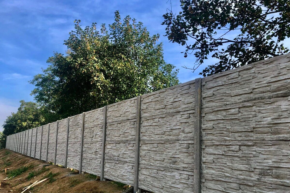 Šedý betonový plot na svažitém pozemku — realizace Stavíme ploty